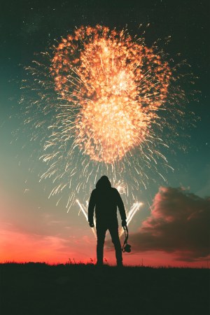 An image of a man at sunset stood in front of a firework display holding a camera